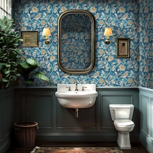 Puede incluir: Un pequeño baño con paredes azules y un papel tapiz floral con pájaros. El baño tiene un lavabo de porcelana blanca, un inodoro y un espejo con marco dorado. Hay dos apliques con bombillas a cada lado del espejo.