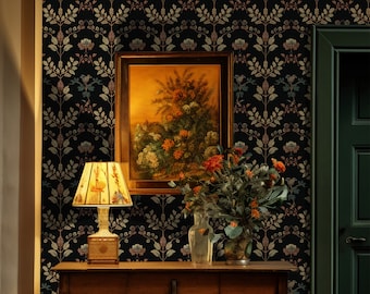 May include: A dark floral wallpaper with a gold and brown pattern. A framed painting of a floral still life hangs on the wall above a wooden table with a lamp and a vase of flowers. A dark green door is to the right of the table.
