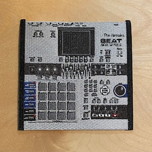 Puede incluir: Parche bordado con un diseño detallado de una máquina de ritmos plateada y negra. El parche tiene un borde negro e incluye el texto "The Breaks BEAT BOX SERIES". El diseño incluye almohadillas, perillas y una pantalla.