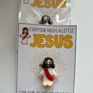 May include: A white card with a cartoon image of Jesus on a cross. The card has the text "Everyone needs a little Jesus" and a quote from Matthew 11:28, "Come to me, all you who are weary and burdened, and I will give you rest."