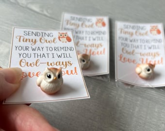 May include: A small, cream-colored owl figurine with orange accents is displayed on a card. The card has the text "SENDING Tiny Owl YOUR WAY TO REMIND YOU THAT I WILL Owl-ways Love You!" Other cards and owl figurines are in the background.