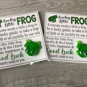 May include: Two white cards with green frog figurines attached. The cards have the text "Lucky Little Frog" and a message about good luck.