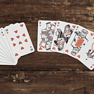 Puede incluir: Una baraja de cartas completa con un tema n&aacute;utico. Las cartas est&aacute;n desplegadas en fila, mostrando los n&uacute;meros del 2 al 10, la sota, la reina, el rey y el as de corazones. Las cartas presentan ilustraciones de marineros, anclas y otras im&aacute;genes n&aacute;uticas.