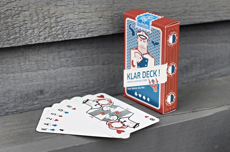Puede incluir: Una baraja de cartas con tem&aacute;tica n&aacute;utica. La caja presenta una ilustraci&oacute;n de dibujos animados de un marinero con un esquema de color rojo y azul. El texto en la caja dice "Klar Deck!" y "Havet Karmmer til Alt".