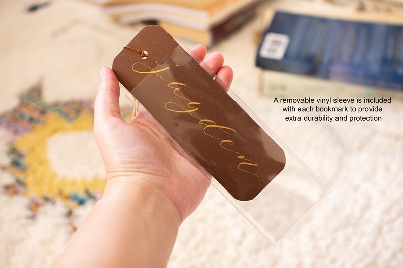 May include: A brown bookmark with a gold inscription that reads "Jayden". The bookmark is in a clear plastic sleeve.