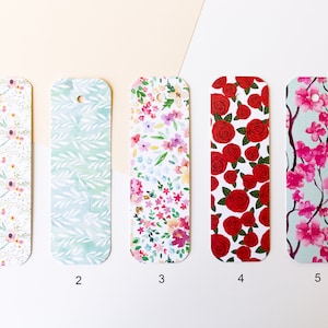 Peut inclure: Cinq designs de signets diff&eacute;rents avec des motifs floraux. Les signets sont rectangulaires avec des coins arrondis et un trou en haut pour accrocher. Les motifs comprennent des fleurs roses et blanches, des feuilles vertes, des roses rouges et des fleurs de cerisier roses.
