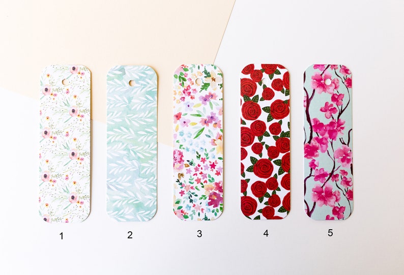 Peut inclure: Cinq designs de signets diff&eacute;rents avec des motifs floraux. Les signets sont rectangulaires avec des coins arrondis et un trou en haut pour accrocher. Les motifs comprennent des fleurs roses et blanches, des feuilles vertes, des roses rouges et des fleurs de cerisier roses.