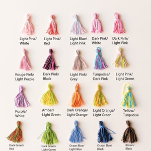 May include: Assortment of 18 colorful yarn tassels with different color combinations. Each tassel is made of soft yarn and has a loop at the top for hanging. The tassels are arranged in three rows of six, with each row featuring a different color scheme.