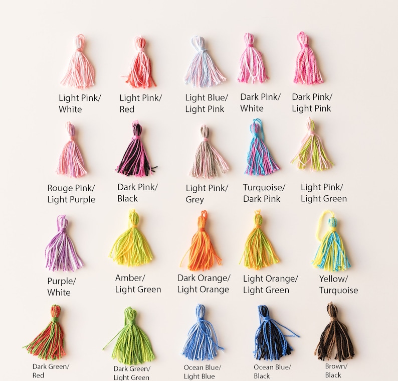 May include: Assortment of 18 colorful yarn tassels with different color combinations. Each tassel is made of soft yarn and has a loop at the top for hanging. The tassels are arranged in three rows of six, with each row featuring a different color scheme.