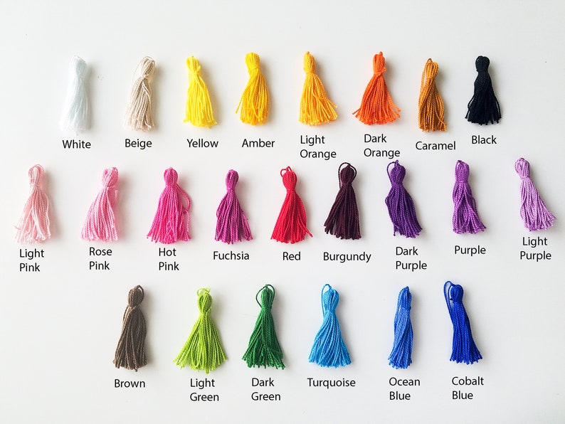 Peut inclure: Une collection de 20 pompons color&eacute;s dans diff&eacute;rentes nuances de blanc, beige, jaune, orange, rouge, rose, violet, marron, vert, bleu et noir. Les pompons sont dispos&eacute;s en rang&eacute;es sur une surface blanche.