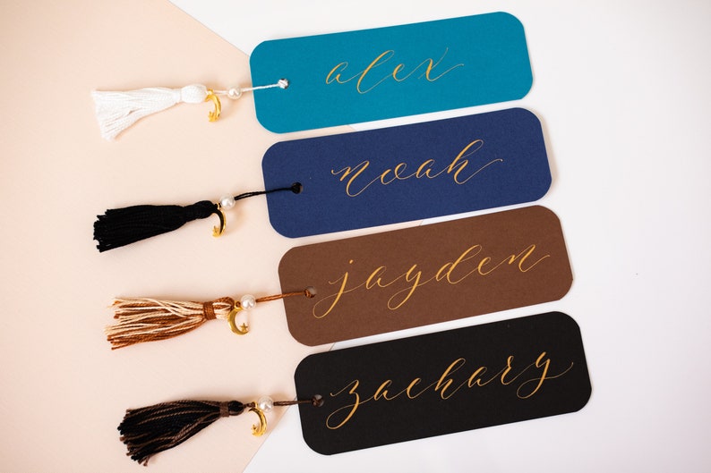 May include: Four personalised bookmarks with gold lettering and tassels. The names on the bookmarks are Alex, Noah, Jayden, and Zachary.