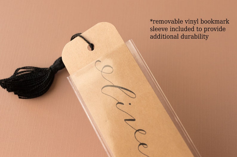 May include: A brown bookmark with the word "divine" written in black cursive script. The bookmark has a black tassel and is protected by a clear vinyl sleeve.