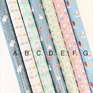 May include: A selection of colorful wrapping paper rolls featuring a repeating pattern of a cartoon bunny character. The rolls are in various colors, including blue, pink, and green, with floral and birthday-themed designs.