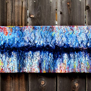 May include: Abstract painting on canvas with blue, white, black, red, and yellow paint. The painting has a textured surface with small dots of paint.