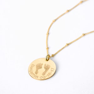 A gold baby footprint disc necklace sits against a white background. Actual baby portrait jewelry, actual baby footprints, baby handprint necklace, baby keepsake jewelry for new mom, loss of baby memorial jewelry for mother, first mothers day gift