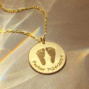 Close-up of personalized footprint necklace on champagne satin fabric, featuring engraved baby feet and name on a gold disc pendant. Available in sterling silver, gold filled, or rose gold filled with cable or satellite chain styles. A meaningful keepsake jewelry piece for new moms, baby shower gifts, push presents, or memorial remembrance necklaces honoring a child’s memory. Minimalist design ideal for everyday wear and sentimental gifting for baby loss gift, memorial present.