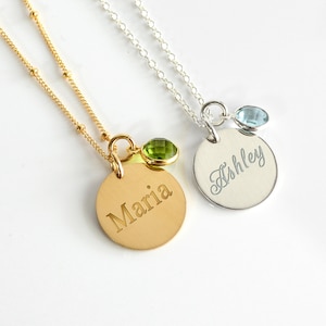 May include: Two gold and silver necklaces with personalized name tags. The gold necklace has a green gemstone charm and says "Maria". The silver necklace has a blue gemstone charm and says "Ashley".