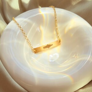 Golden heartbeat bar necklace on satin with prism glow; personalized ultrasound soundwave engraving, option to add name and birth date on reverse; fine 14k gold filled chain, minimalist layering necklace; pregnancy reveal, new mama gift, push present.