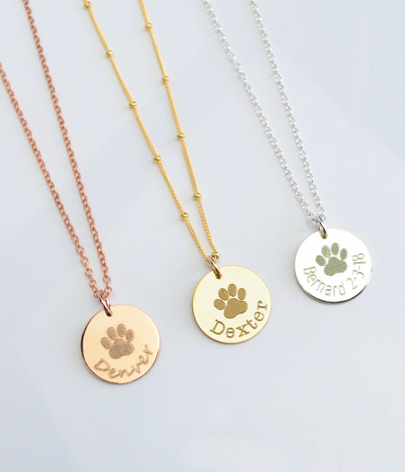 A rose gold, a gold filled and a sterling silver necklace all next to each other. Each is engraved with a paw print and a name. The chains are an assortment of cable and satellite chains. Pet name necklaces, pet name jewelry