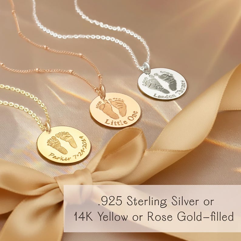 Three baby footprint necklaces in gold, rose gold, and silver hanging in warm sunlight near a window. Each round pendant features engraved footprints and custom text, showcasing personalized newborn keepsake jewelry in a soft, glowing setting.