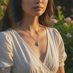 Woman wearing a blue baguette birthstone bar necklace on a delicate gold chain, holiday bokeh background—minimalist pendant with optional hidden engraving; elegant personalized gift for her.