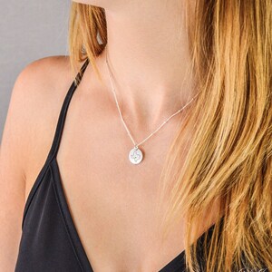 May include: A silver necklace with a small round pendant featuring an outline of the state of Texas. The necklace is worn by a person with long blonde hair.