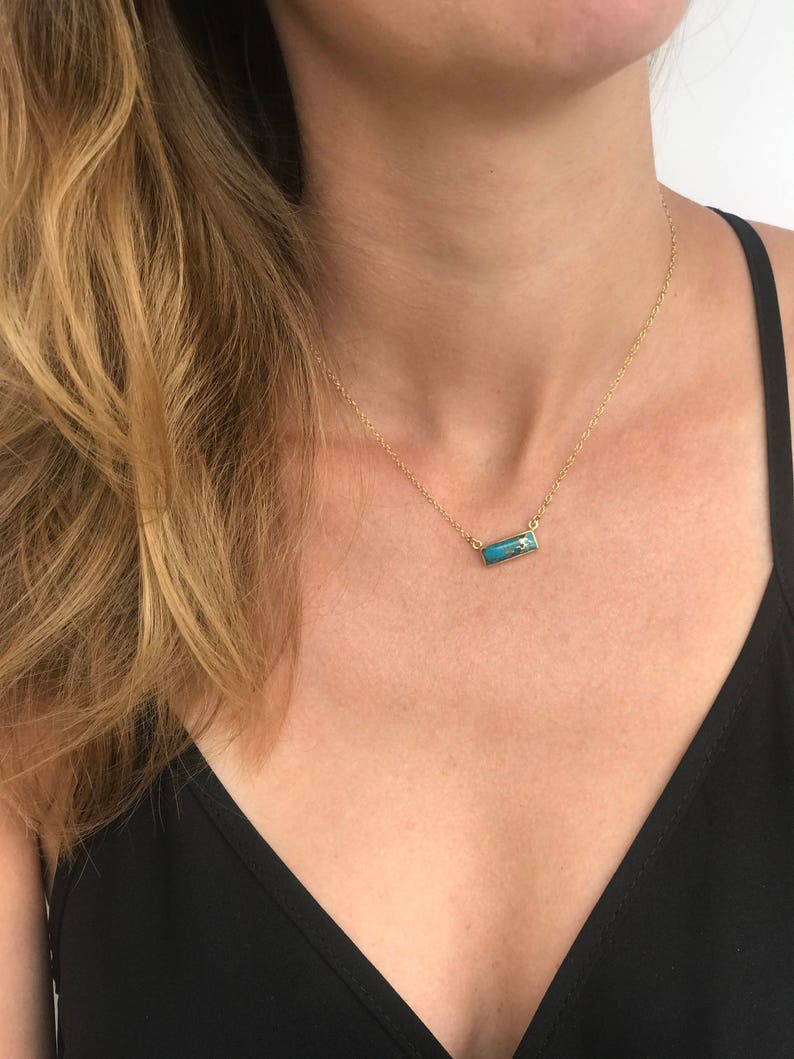 A person in a black v neck shirt wears a copper turquoise bar necklace set in silver. Turquoise necklace, natural turquoise necklace, copper turquoise necklace, handmade jewelry, handmade turquoise necklace, december birthstone jewelry