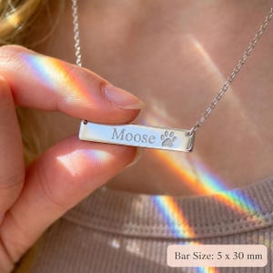 Close-up of silver paw print bar necklace engraved with pet name Moose, showing 5 x 30 mm bar pendant size.