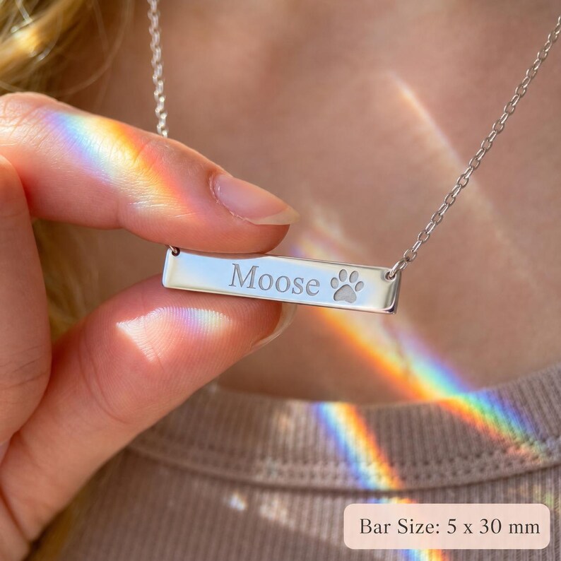 Close-up of silver paw print bar necklace engraved with pet name Moose, showing 5 x 30 mm bar pendant size.