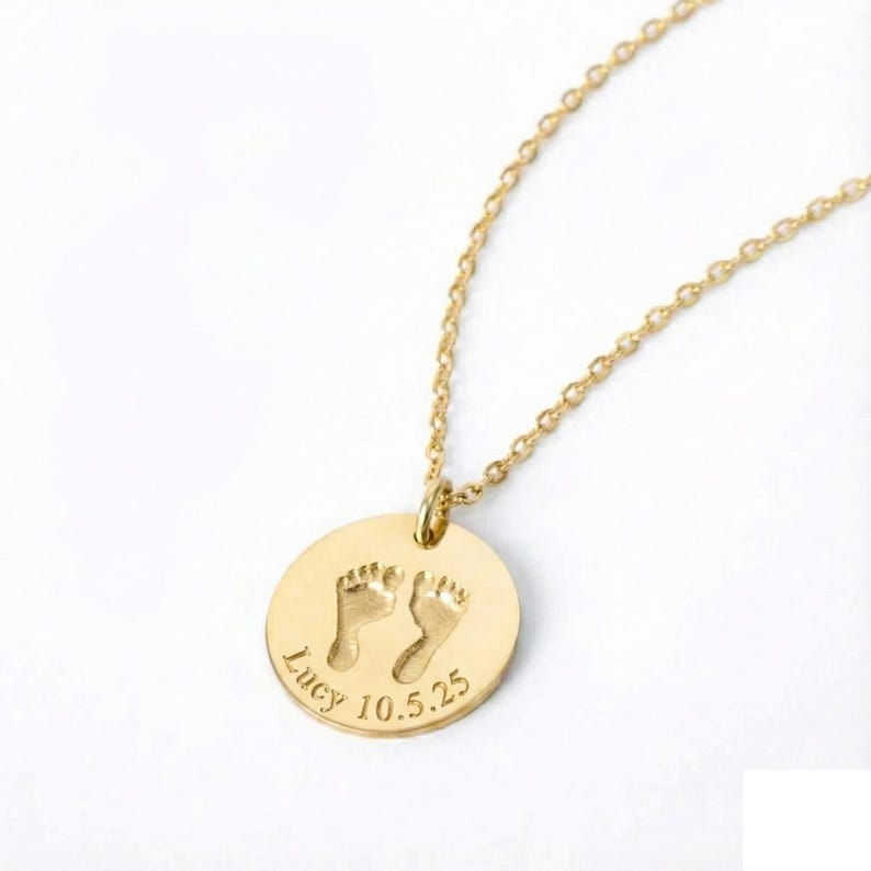 Gold baby footprint necklace featuring a round engraved pendant with tiny footprints, personalized name, and birthdate. Shown on a white background to highlight the delicate chain and custom engraving, perfect for new moms and keepsake gifts