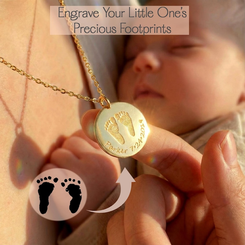 Mother gently holding her sleeping newborn while wearing a gold baby footprint necklace engraved with a name and date. The close-up highlights the sentimental personalized pendant and the intimate moment between mom and baby, capturing a meaningful keepsake.