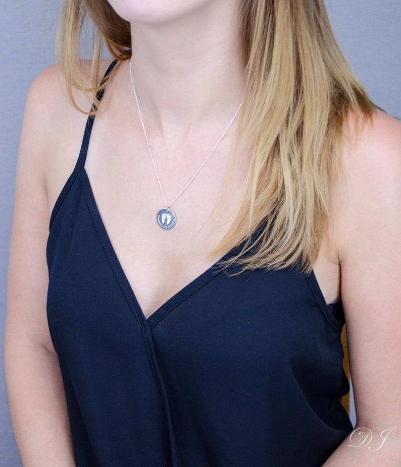 A woman with pale skin and a black v-neck tank top. She is wearing an engraved footprint disc necklace.Engraved disc necklace, custom baby necklace, Mothers Day gifts, Christmas gifts, gift for new mom, gift for grandma, silver jewelry, gold jewelry