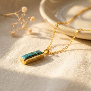 Turquoise birthstone necklace with hidden engraved message displayed on a soft neutral background.