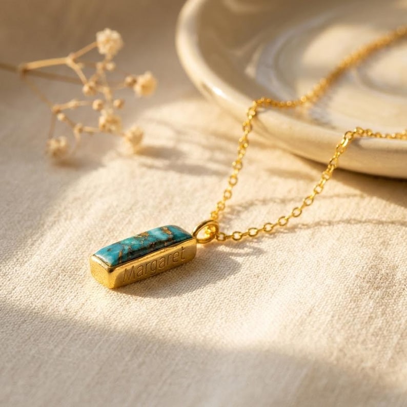 Turquoise birthstone necklace with hidden engraved message displayed on a soft neutral background.