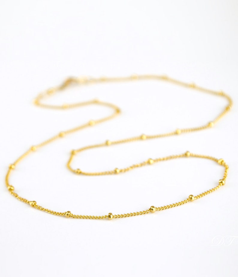 This image shows a 14” yellow gold satellite chain. The chain is lying flat on a surface with the closest part of the chain more clearly in focus. Pairs well with our teardrop gemstone pendants, large oval pendants and disc charms.