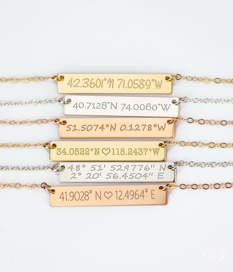 May include: Five gold, silver, and rose gold necklaces with bar pendants engraved with latitude and longitude coordinates. The pendants are engraved with different coordinates, including 42.3601&deg;N 71.0589&deg;W, 40.7128&deg;N 74.0060&deg;W, 51.5074&deg;N 0.1278&deg;W, 34.0522&deg;N 118.2437&deg;W, 48&deg; 51' 52.9776" N 2&deg; 20' 56.4504" E, and 41.9028&deg; N 12.4964&deg; E.