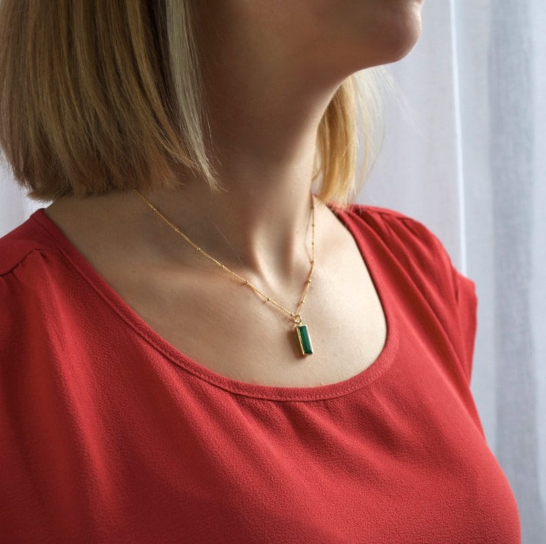 A woman with pale skin and a red scoop neck t shirt. She is wearing a vertical green onyx engraved bar necklace which rests near her collarbone. Birthstone necklace, bridesmaid jewelry, wedding gifts, Mother’s Day gifts, Christmas gifts, thank you