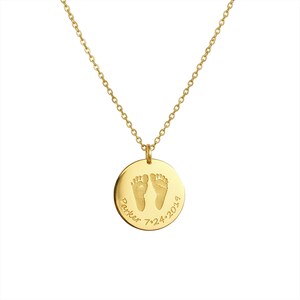 Gold round pendant necklace engraved with tiny baby footprints and the name ‘Parker’ with a birthdate, displayed on a clean white background.