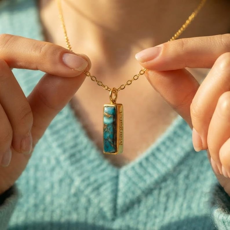 Model holding a turquoise necklace pendant to show the engraved side message detail.