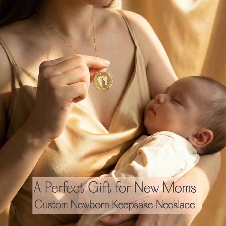 Mother holding a sleeping newborn while gently touching her gold baby footprint necklace engraved with a name and date.