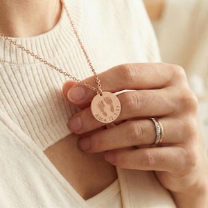 Minimalist baby footprint necklace with a polished round pendant engraved with tiny footprints and customizable text. Designed for everyday wear, this simple and elegant piece makes a beautiful keepsake for moms who love personalized, meaningful jewelry -just in time for Christmas. She will love this as a stocking stuffer gift!