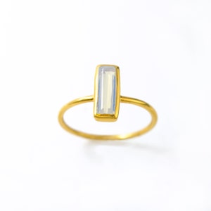 May include: A gold ring with a clear rectangular gemstone. The ring is simple and elegant.