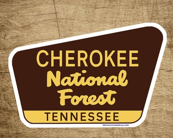 May include: A brown and white sticker with the text "Cherokee National Forest Tennessee" in yellow lettering. The sticker is shaped like a rounded rectangle with a pointed top.