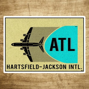 May include: A vintage-style illustration of an airplane flying into a blue circle with the text "ATL" and the words "Hartsfield-Jackson Intl." below.