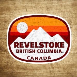 May include: A white and red vintage-style sticker with a mountain range and a sun. The sticker says "Revelstoke British Columbia Canada".
