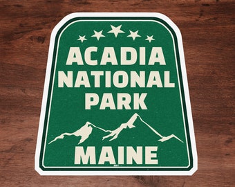 May include: A green and white sticker with the text "Acadia National Park Maine" and a silhouette of mountains. Five white stars are above the text "Acadia National Park".
