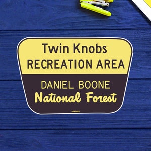 May include: Yellow and brown sign with the text "Twin Knobs Recreation Area Daniel Boone National Forest".