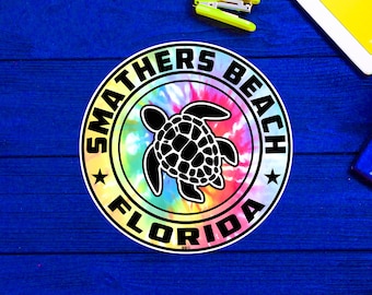 Può includere: Un adesivo tie-dye colorato con una silhouette di tartaruga marina nera al centro. L'adesivo dice "Smathers Beach Florida" in un cerchio bianco attorno alla tartaruga.