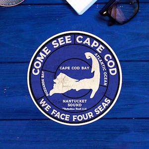 May include: A blue and white round sticker with the text "Come See Cape Cod" and a map of Cape Cod. The text "We Face Four Seas" is also on the sticker.