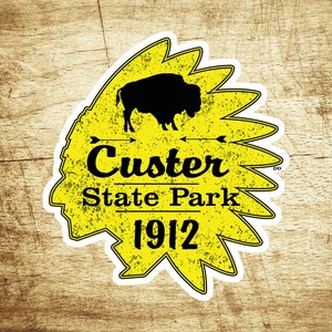 May include: Yellow sticker with a black silhouette of a buffalo and the text "Custer State Park 1912" inside a stylized Native American headdress.
